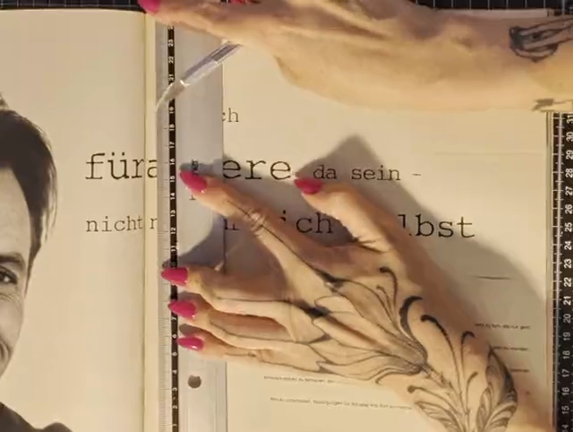 The first frame of the cutting video: the uncut magazine page, a steel ruler laid vertically along the line to be cut, a hand steadying the paper, the typeset German line partly hidden behind hand and shadow.