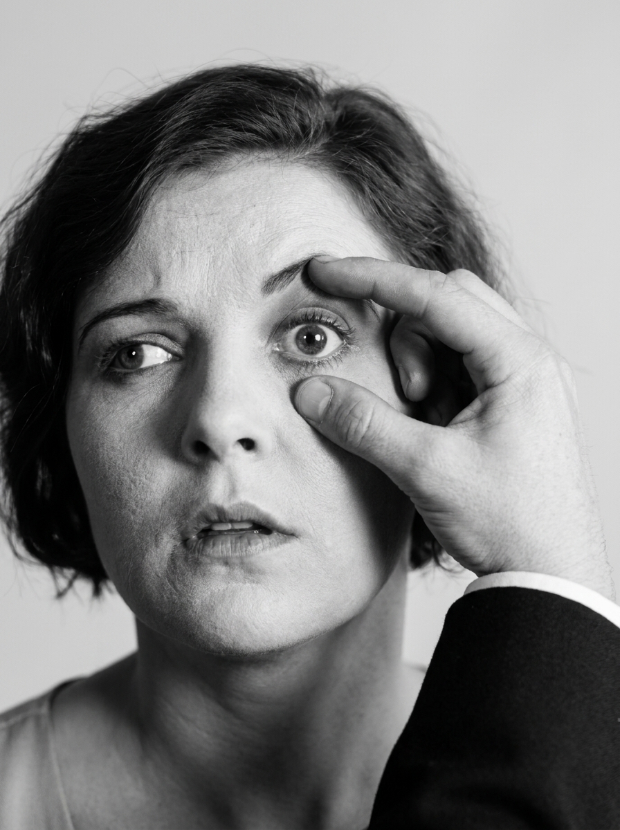 A woman’s face close up in black and white, with somebody else’s hand reaching in from the right to hold one of her eyes open.